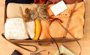 Vista de cima de uma mala aberta, exibindo roupas em tons terrosos, câmera, fones de ouvido e outros acessórios de viagem organizados